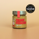 A glass jar of Rhythm 108 Creamy Pistachio Spread with a silver lid and a red seal, set against a solid beige background with a 'great taste 2026' award badge in the top right corner.