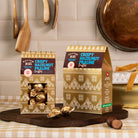 Two boxes of rhythm 108 crispy hazelnut praline truffles  on a kitchen counter with utensils in the background.