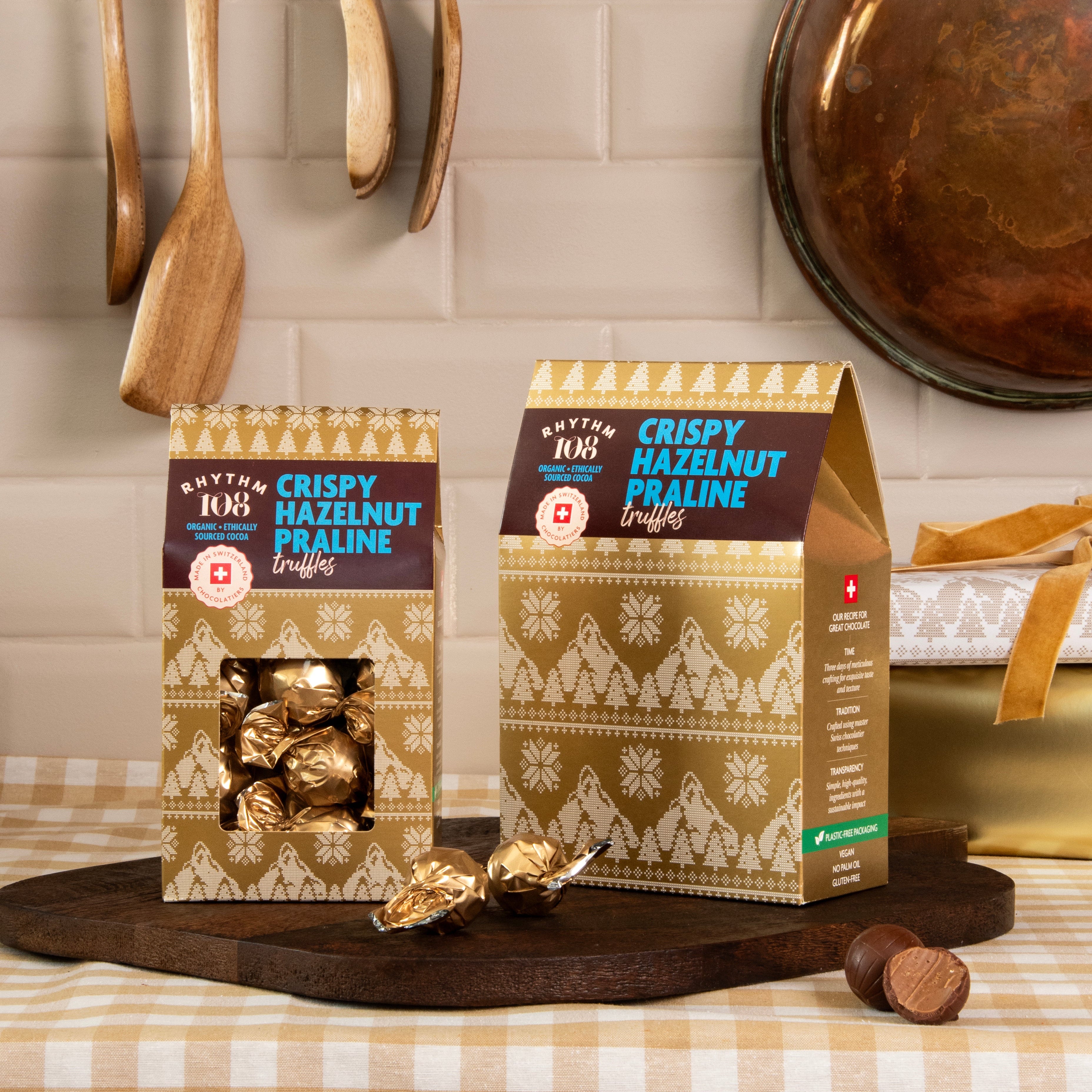 Two boxes of rhythm 108 crispy hazelnut praline truffles  on a kitchen counter with utensils in the background.